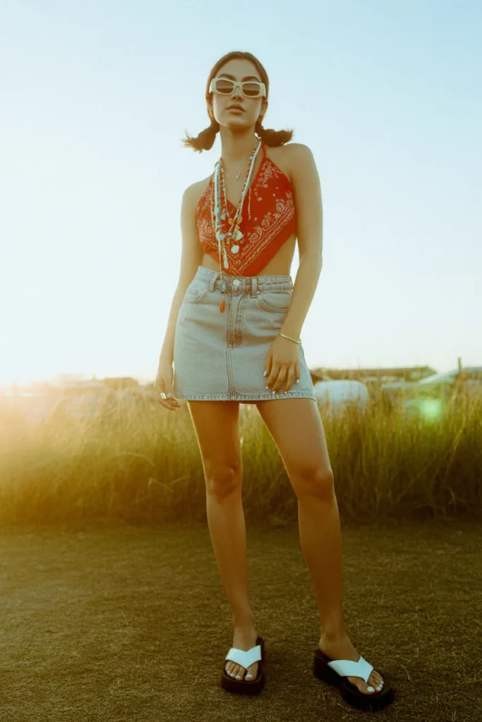 Y2K summer outfit with bandana halter top, denim mini skirt, and platform flip-flops at a festival.